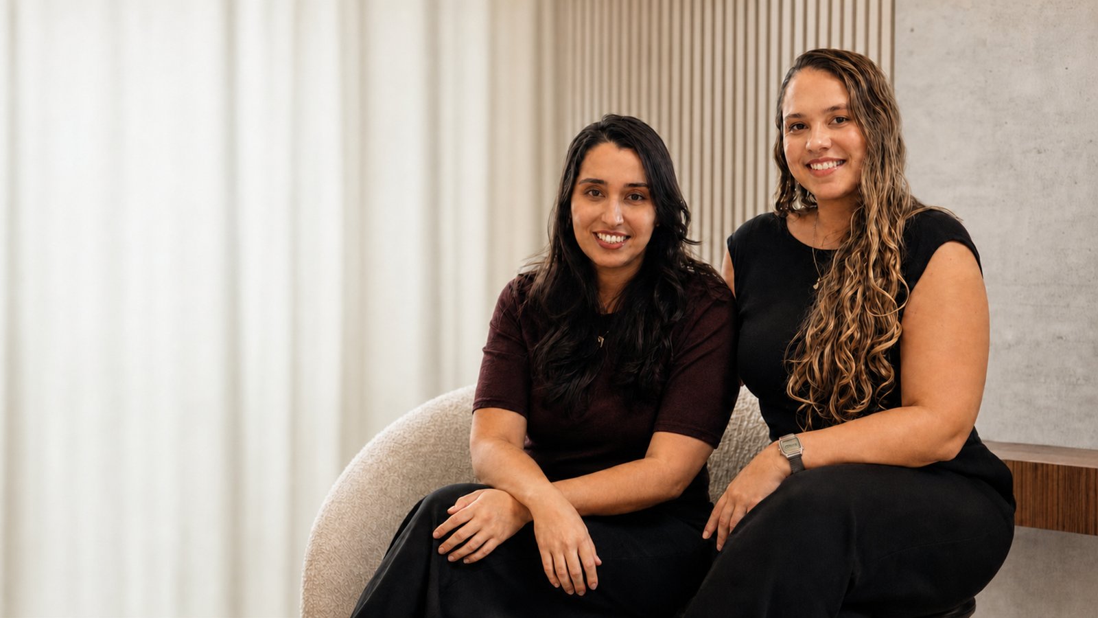 Isis Barbosa e Anna Botsis em um retrato profissional, sentadas em um ambiente contemporâneo da IBA Arquitetura.